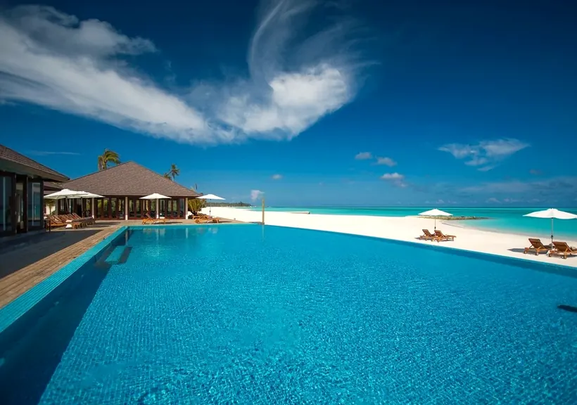 An outdoor pool next to a white sand beach